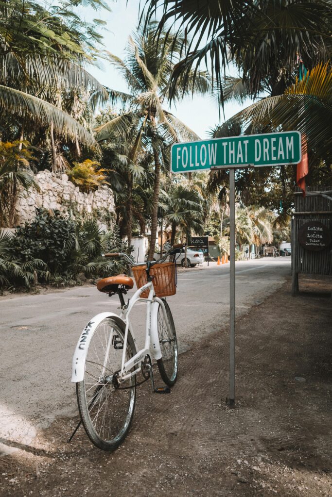 A bicycle near an inspirational sign 'Follow That Dream' in Tulum, Mexico with palm trees around.