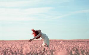 Woman with red hair in a white dress expressing freedom in a vibrant summer field.