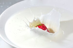 Detailed image of a strawberry splashing into fresh milk, creating a high-impact splash effect.