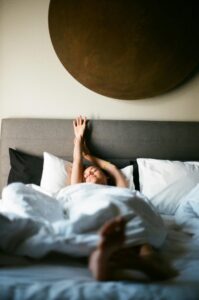 A person comfortably stretching in bed, basking in morning light.